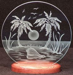 a glass plate with palm trees and a boat in the water on a wooden stand