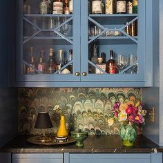 a kitchen with blue cupboards and glass shelves filled with liquor bottles on the counter