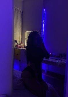 a woman sitting in front of a mirror with blue lights on it's walls