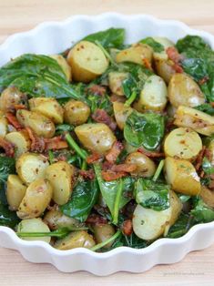 a white bowl filled with spinach and potatoes on top of a pink table cloth