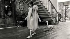 an old photo of a woman standing in front of a staircase with a goose on the floor