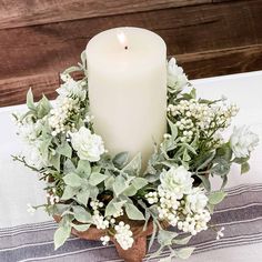 a white candle sitting on top of a wooden stand filled with flowers and greenery