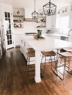 a white kitchen with wooden floors and lots of stools around the island countertop