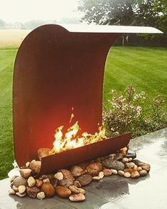 an outdoor fire pit with rocks on the ground and grass in the backround