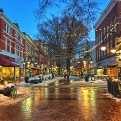 a city street is covered in snow and lit up with christmas lights on the buildings