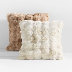 two pillows with fluffy fur on them sitting next to each other in front of a white wall