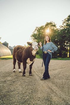 a woman standing next to a cow on a dirt road