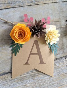 paper flowers are placed on top of a brown card with the letter a in it