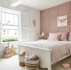 a white bed sitting next to a window with pink walls and pillows on top of it