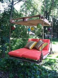 an outdoor swing bed in the middle of some bushes and trees with pillows on it