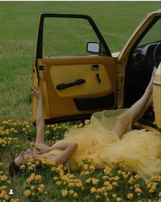 a woman laying in the grass next to a yellow truck with her hand on the door