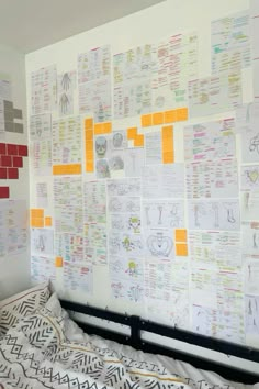 a bed sitting in front of a white wall covered in lots of papers and sticky notes