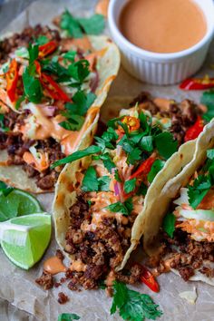 three tacos with meat, vegetables and sauces on a piece of parchment paper