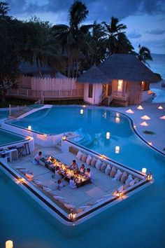 an outdoor dining area next to a swimming pool at night with candles on the tables