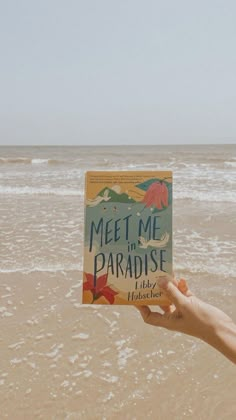 someone holding up a book on the beach