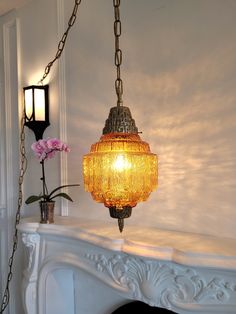 a light hanging from a chain over a fire place with flowers on the mantel