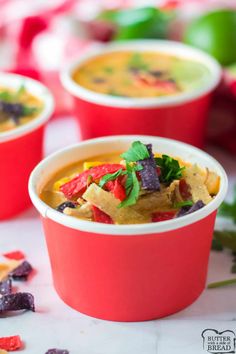 a red cup filled with soup and vegetables on top of a table next to other bowls