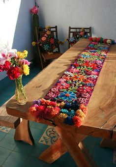 a wooden table topped with colorful crocheted rugs next to vase filled with flowers