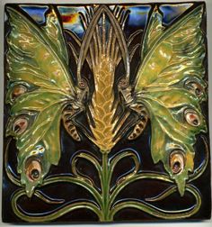 a decorative tile with green leaves and two birds on the front, against a black background