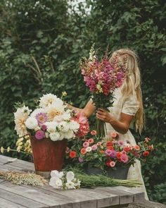 a woman arranging flowers on top of a wooden table