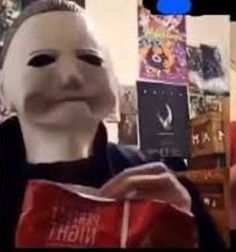 a person wearing a mask and holding a red gift box in front of a christmas tree