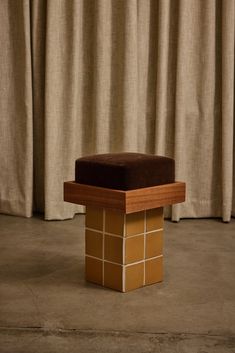 a brown ottoman sitting on top of a cement floor next to a curtained window