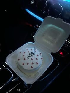 a cake in a plastic container sitting on top of a car dash board next to an air vent