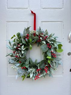 a wreath hanging on the front door of a house with red berries and green leaves