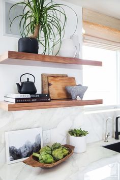 two wooden shelves with plants and pictures on them in a white kitchen countertop area