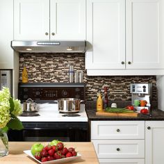 a kitchen with white cabinets and black counter tops, stainless steel appliances and fruit on the table