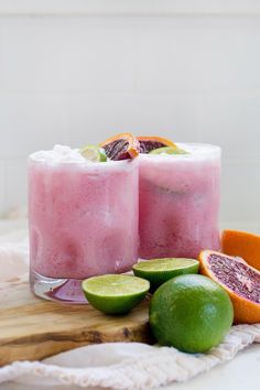 two glasses filled with pink and green drinks next to sliced oranges on a cutting board