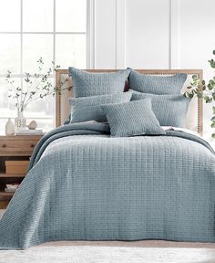 a bed with blue comforters and pillows in a room next to a plant on a table