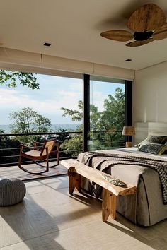 a bedroom with a bed, chair and large window overlooking the trees in the distance