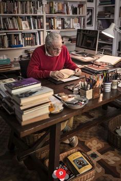 an older woman sitting at a desk with books and pens in front of her on the table