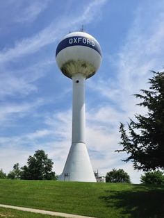 a large white water tower sitting on top of a lush green field under a blue sky