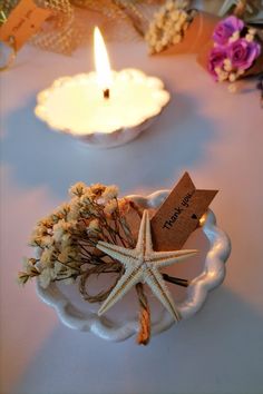 a starfish on a plate next to a lit candle and some dried flowers in a bowl