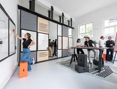 a group of people standing around a whiteboard in a room with black and orange accents