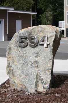 a large rock with the number 594 on it in front of a building and trees