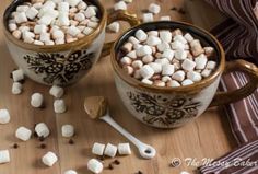 two mugs filled with marshmallows on top of a wooden table