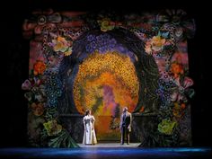 two people standing on a stage in front of an artistic backdrop with flowers and leaves