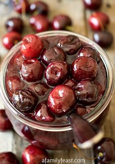 a glass jar filled with cherries sitting on top of a wooden table next to other cherries