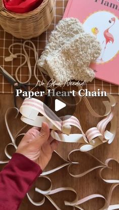 someone cutting out paper hearts with scissors on top of a wooden table next to a book