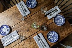 a wooden table topped with blue and white plates next to silverware on top of it