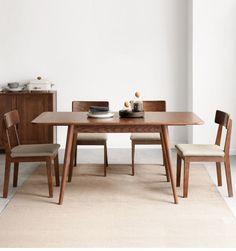 a wooden table with two chairs and a bowl on it, in front of a white wall