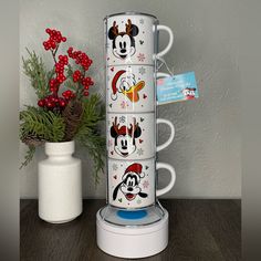 mickey mouse mugs are stacked on top of each other in front of a potted plant