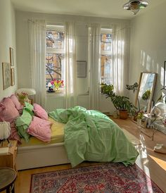 a bedroom with a bed, rugs and plants in the window sill area