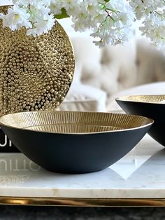 two black bowls sitting on top of a table next to a vase with white flowers