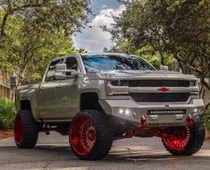 a silver truck with red rims parked on the street in front of some trees