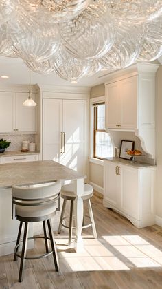 a kitchen with white cabinets and an island in the middle, surrounded by stools