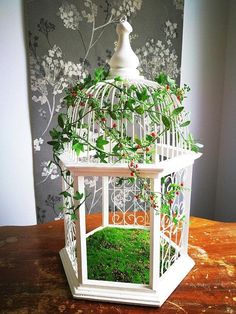 a white birdcage with plants growing out of it's sides on a table